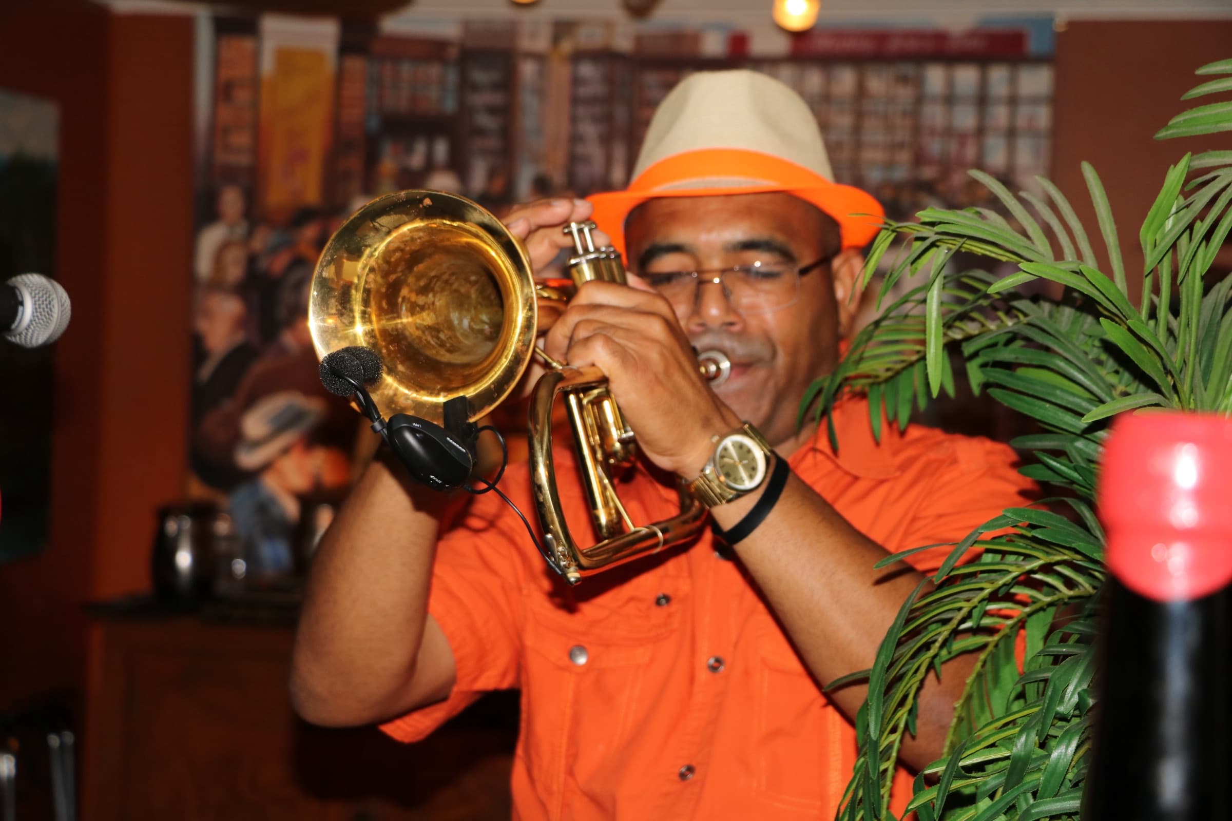 A trumpet player in an orange shirt and straw fedora performing in the dining room