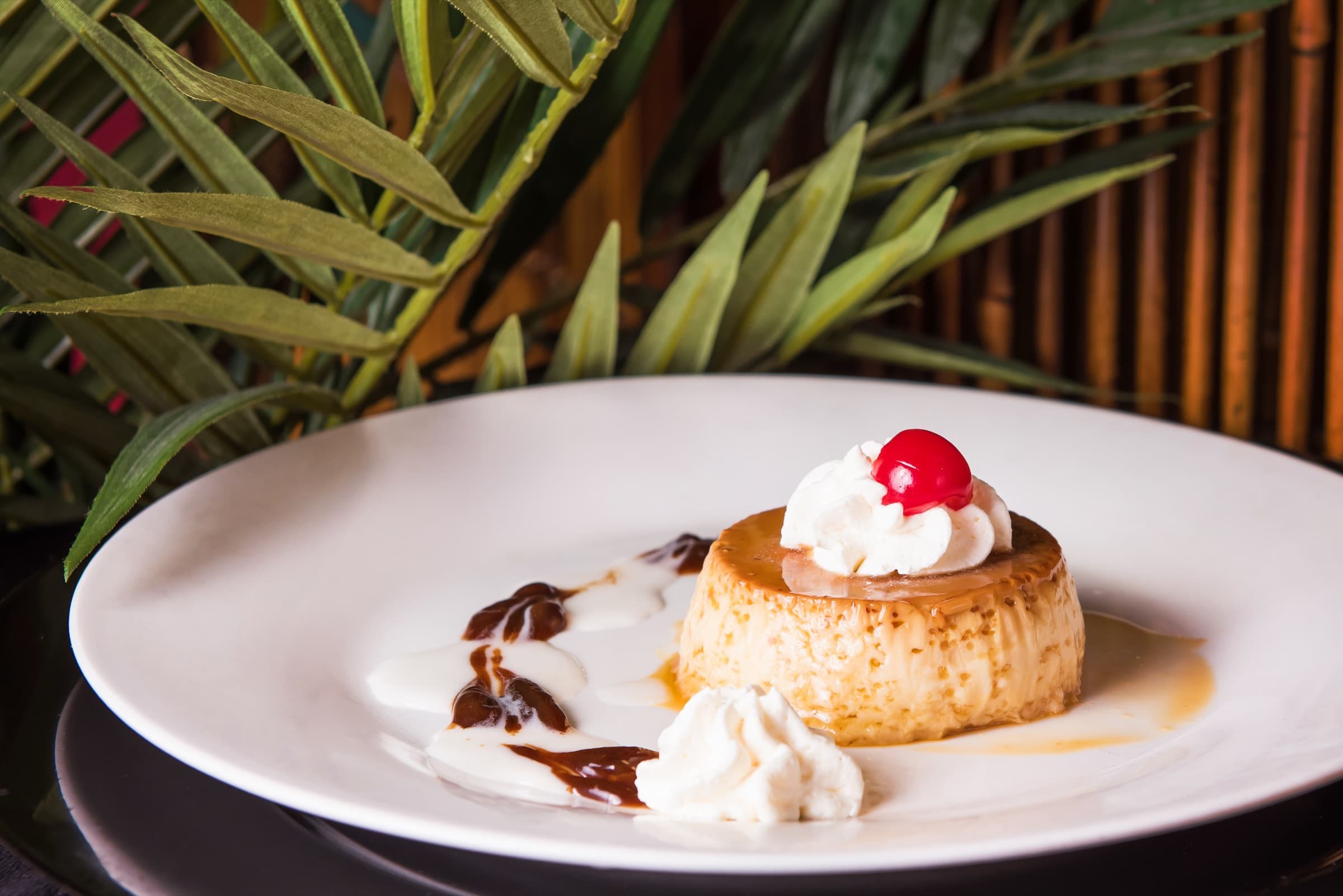 Flan de la casa under caramel with whipped cream and a cherry, on a white plate