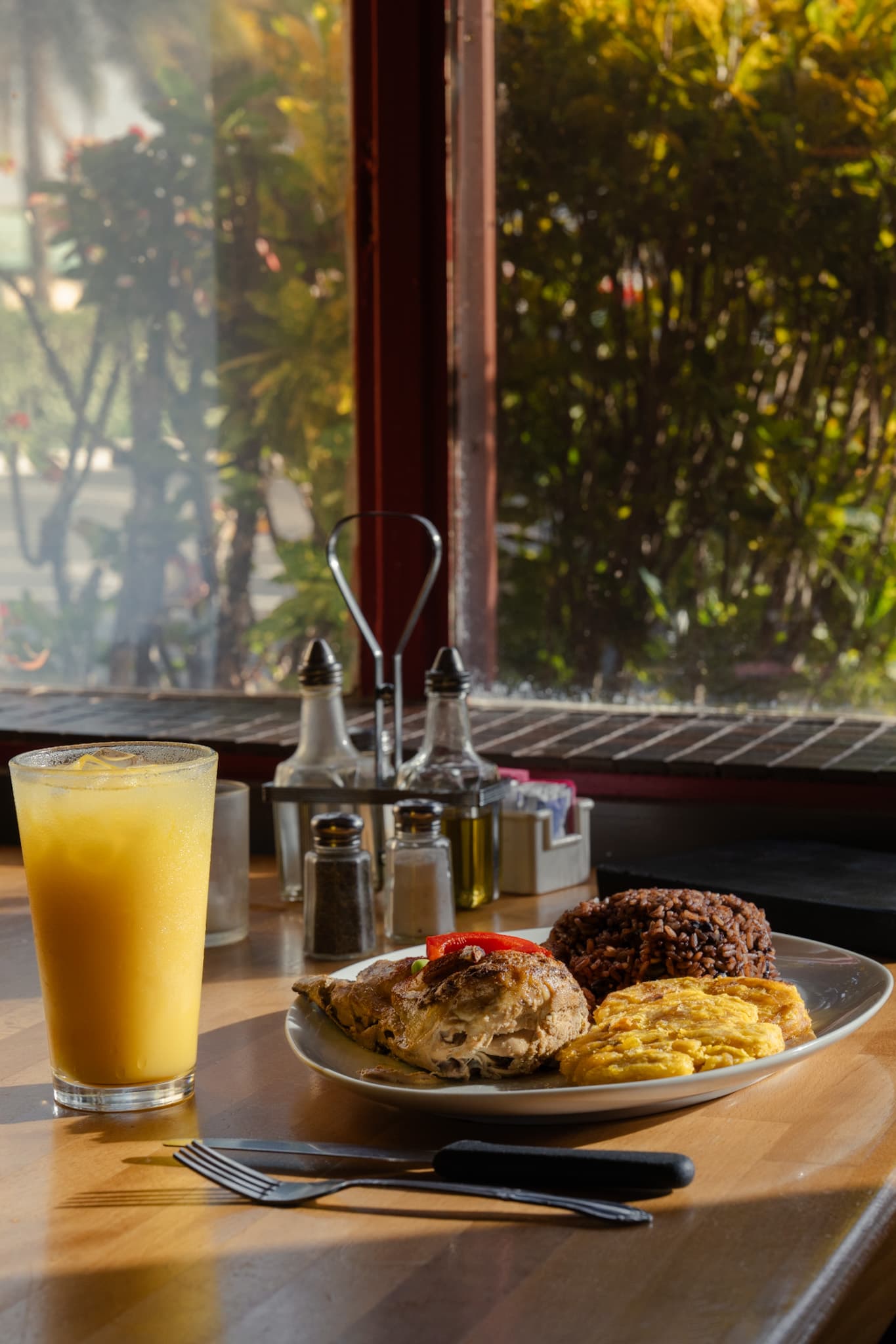 A Cuban lunch plate and fresh juice at a sunlit window table
