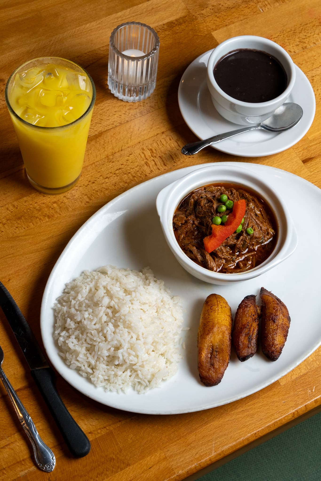 Beef stew with white rice and sweet plantains, black bean soup and orange juice alongside